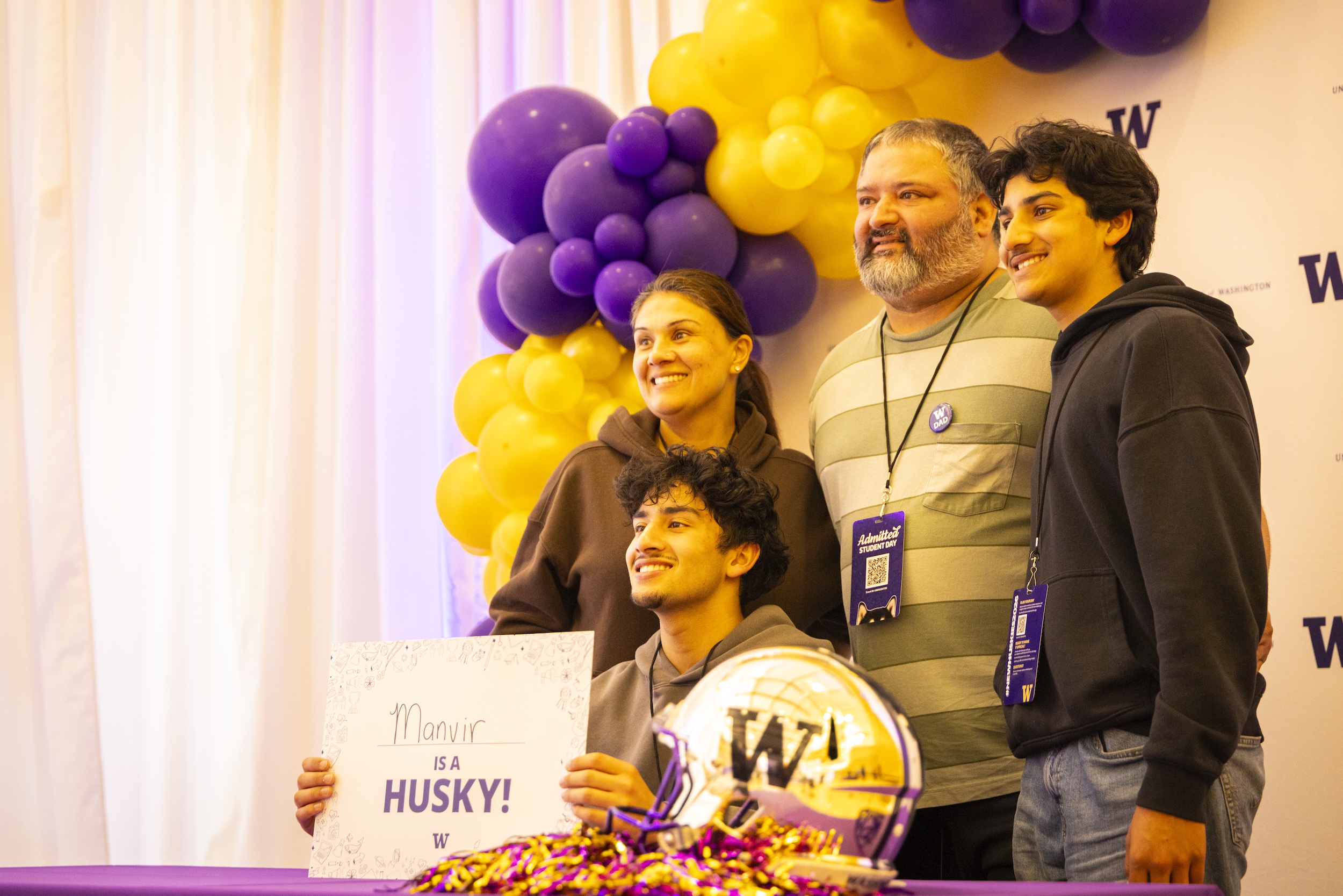 Student smiling with their family, holding a commit sign at Admitted Student Day