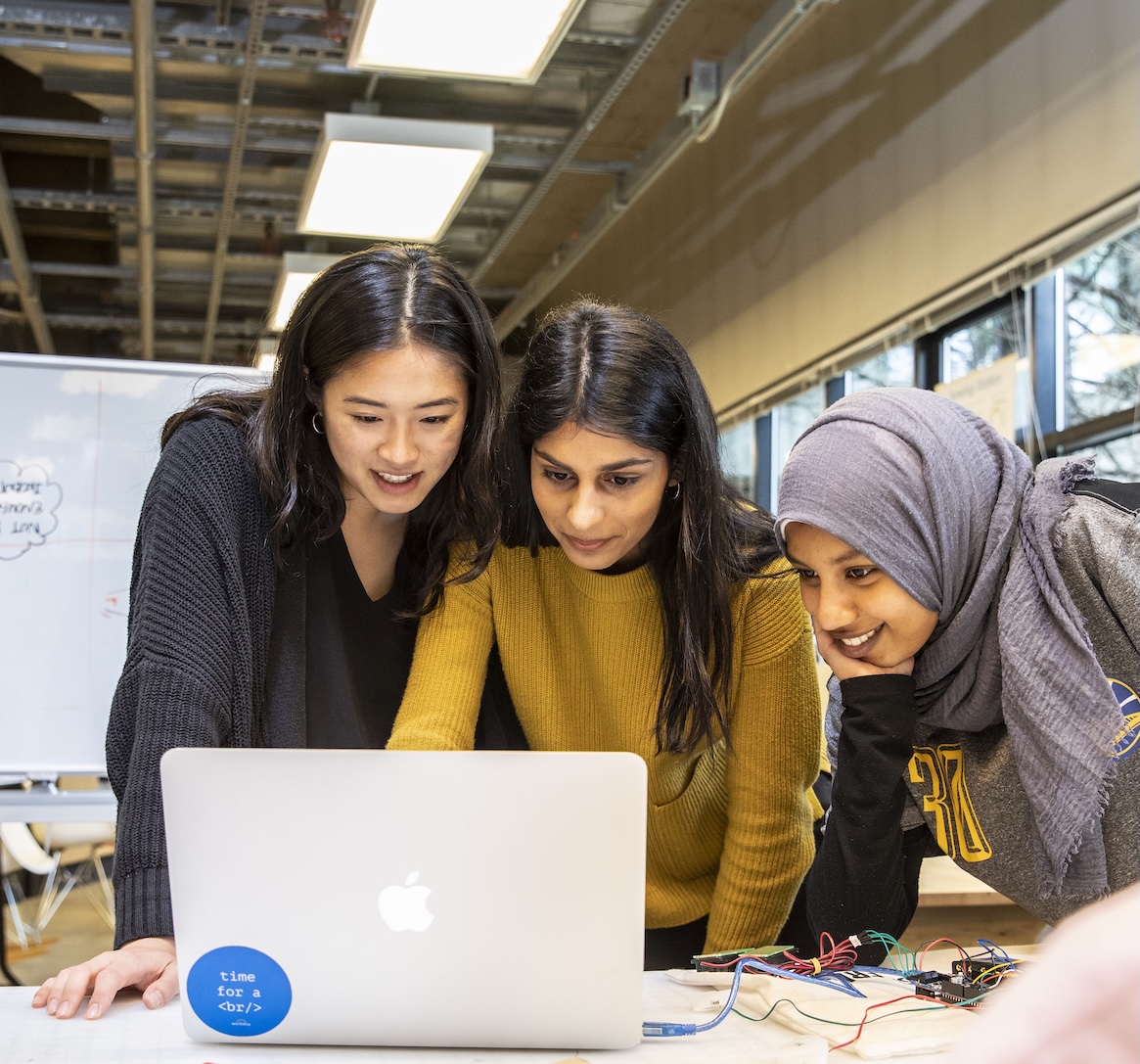 three students looking at an open laptop screen together, smiling