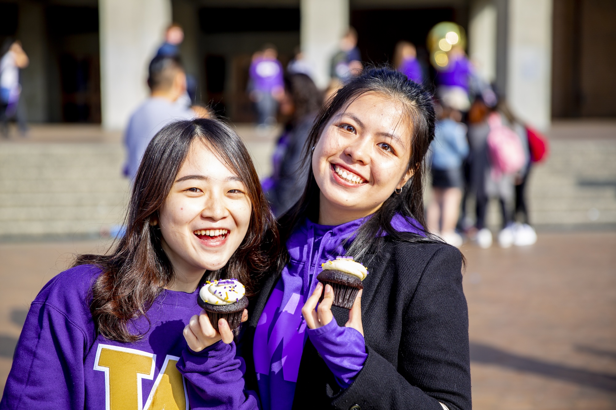 two students dressed in husky gear holding UW themed cupcakes