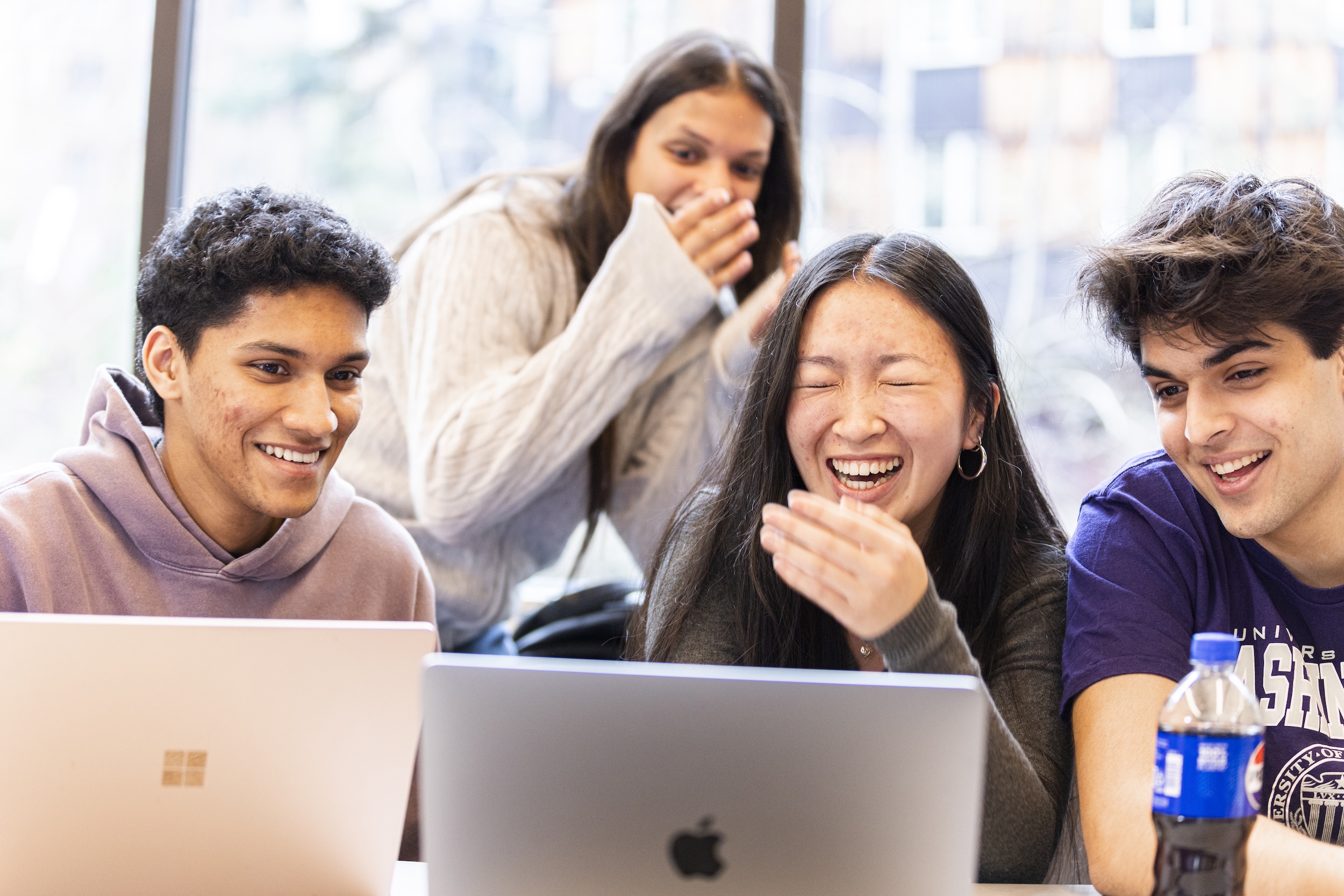 Students all looking at their laptops together, smiling. 