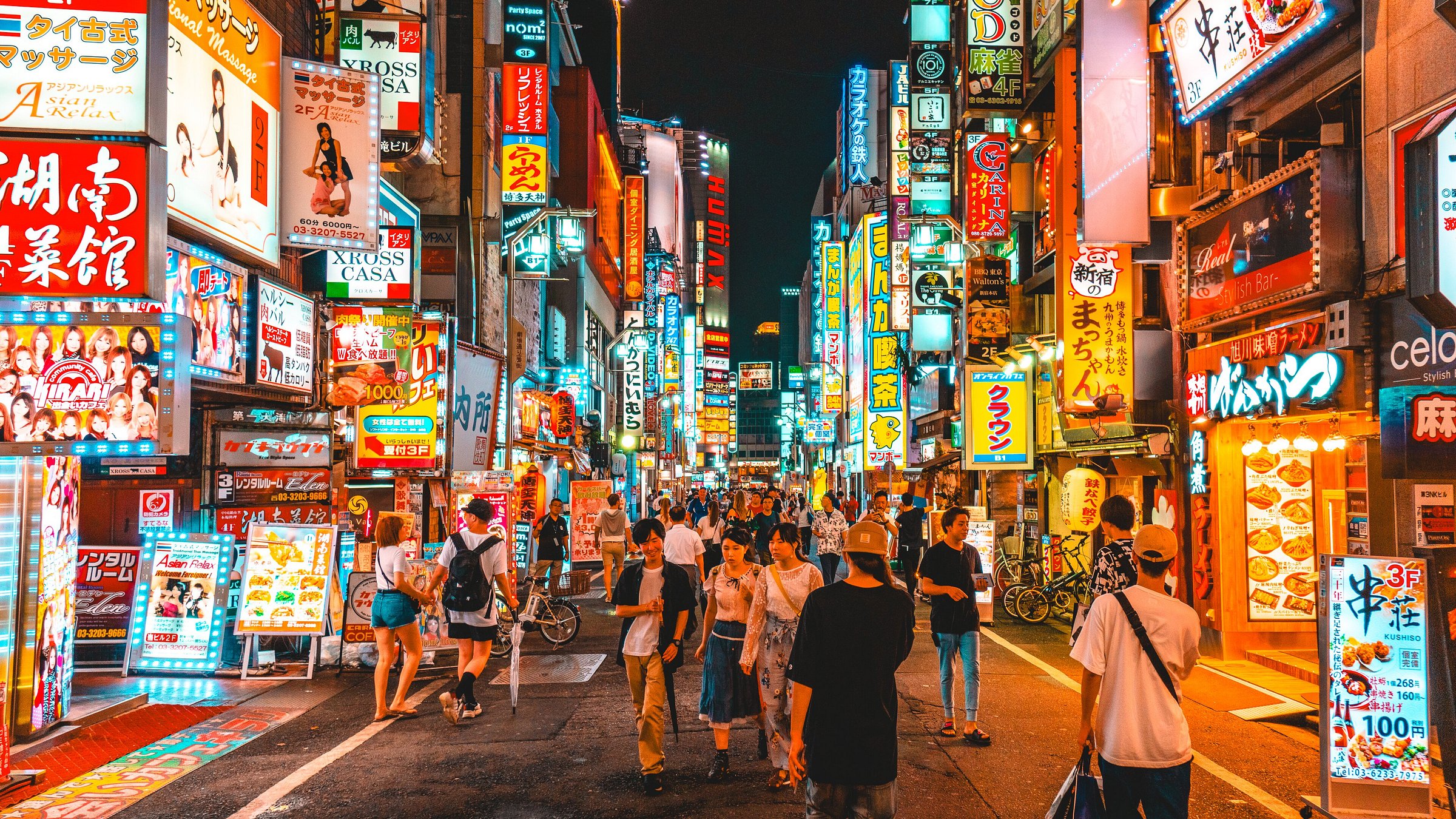 A lit-up Tokyo street at night with young people walking around.